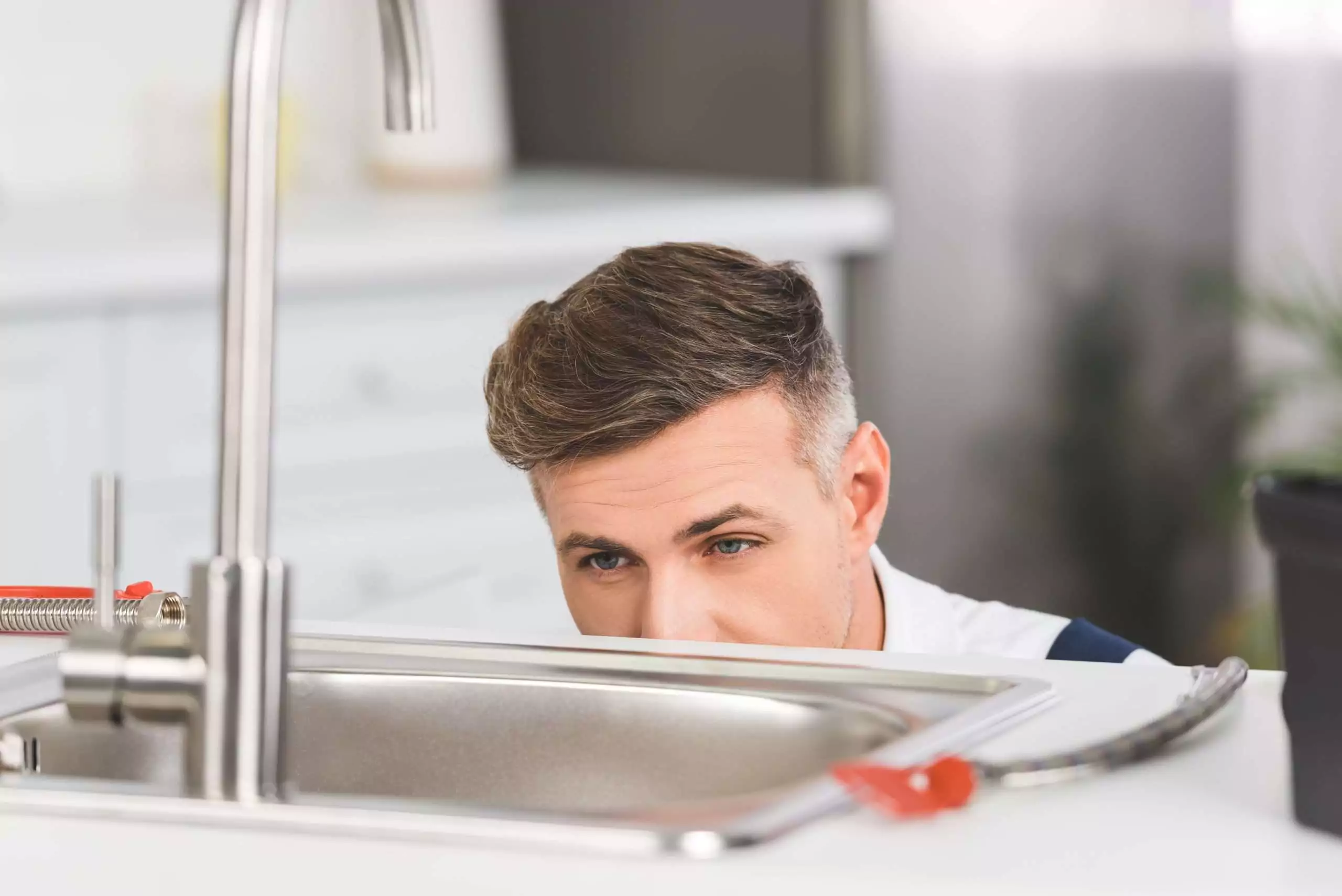 cropped view of adult repairman looking at sink at kitchen