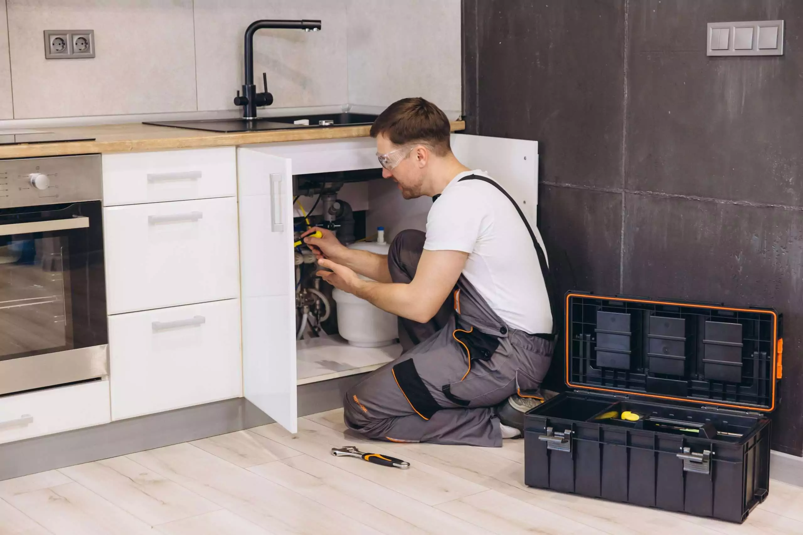 Plumber Working Under Sink in Modern Kitchen