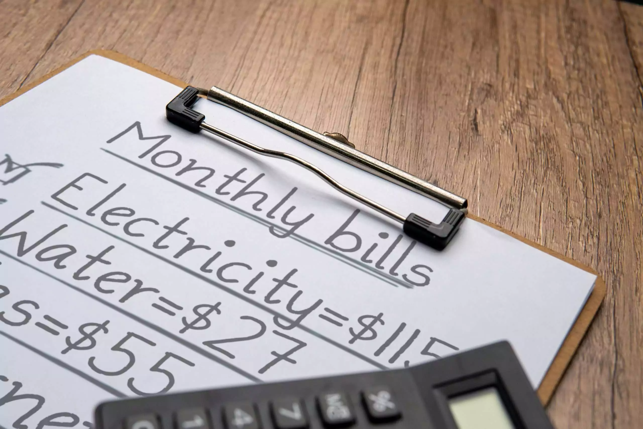 Monthly Bills List with Calculator on Wooden Surface