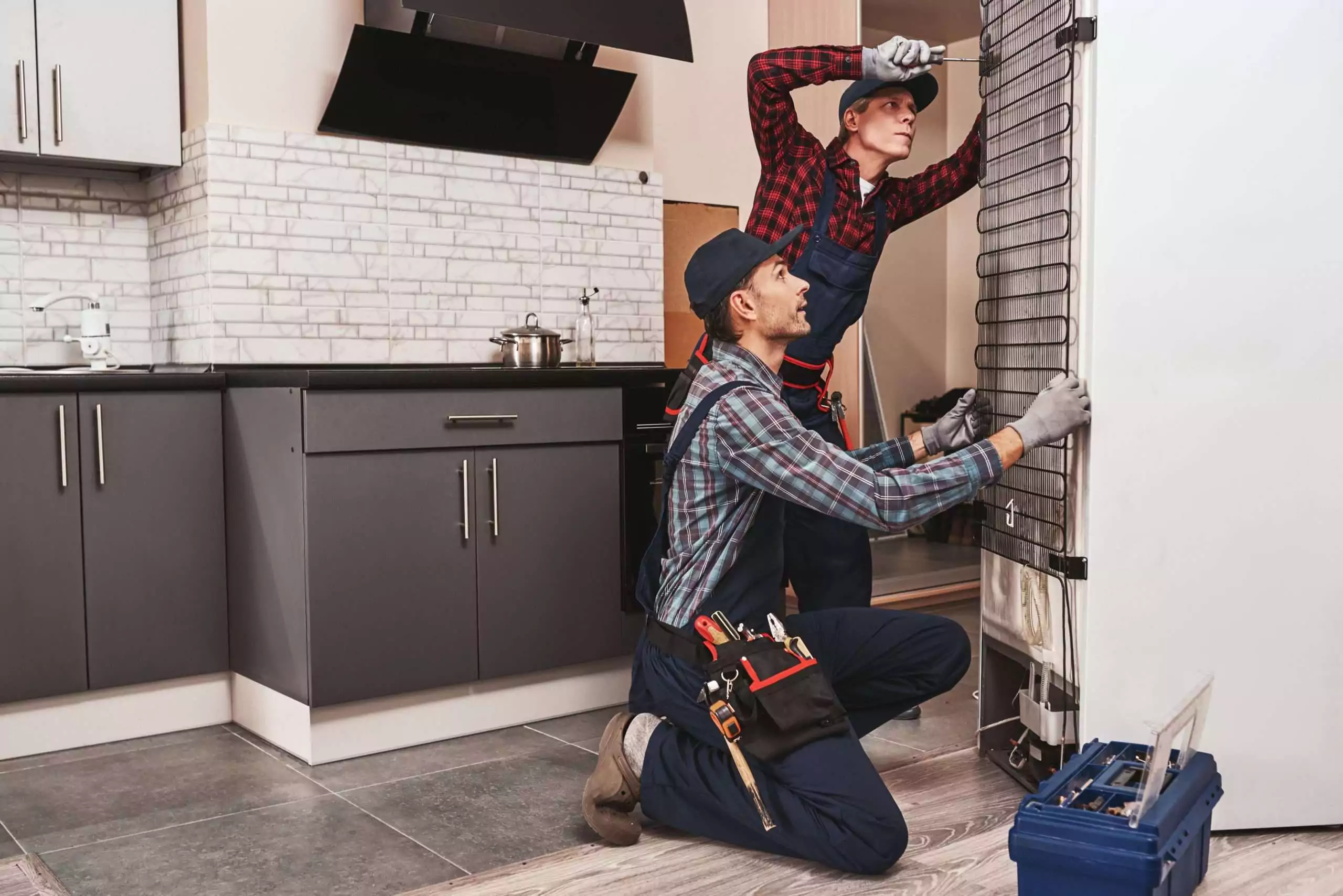 Technicians Repairing a Refrigerator in a Home Kitchen