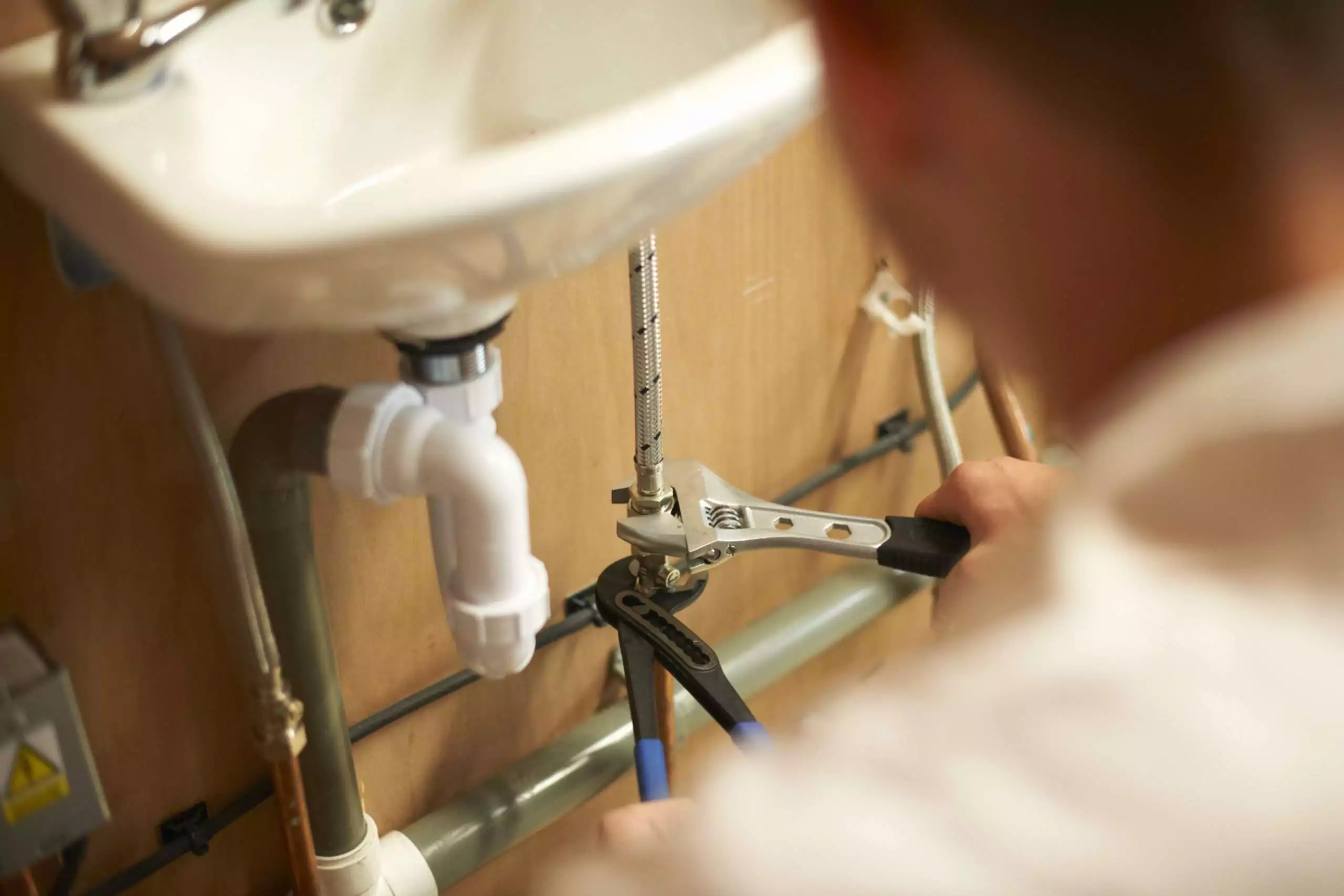 Male trainee plumber using adjustable spanner on pipework in college workshop