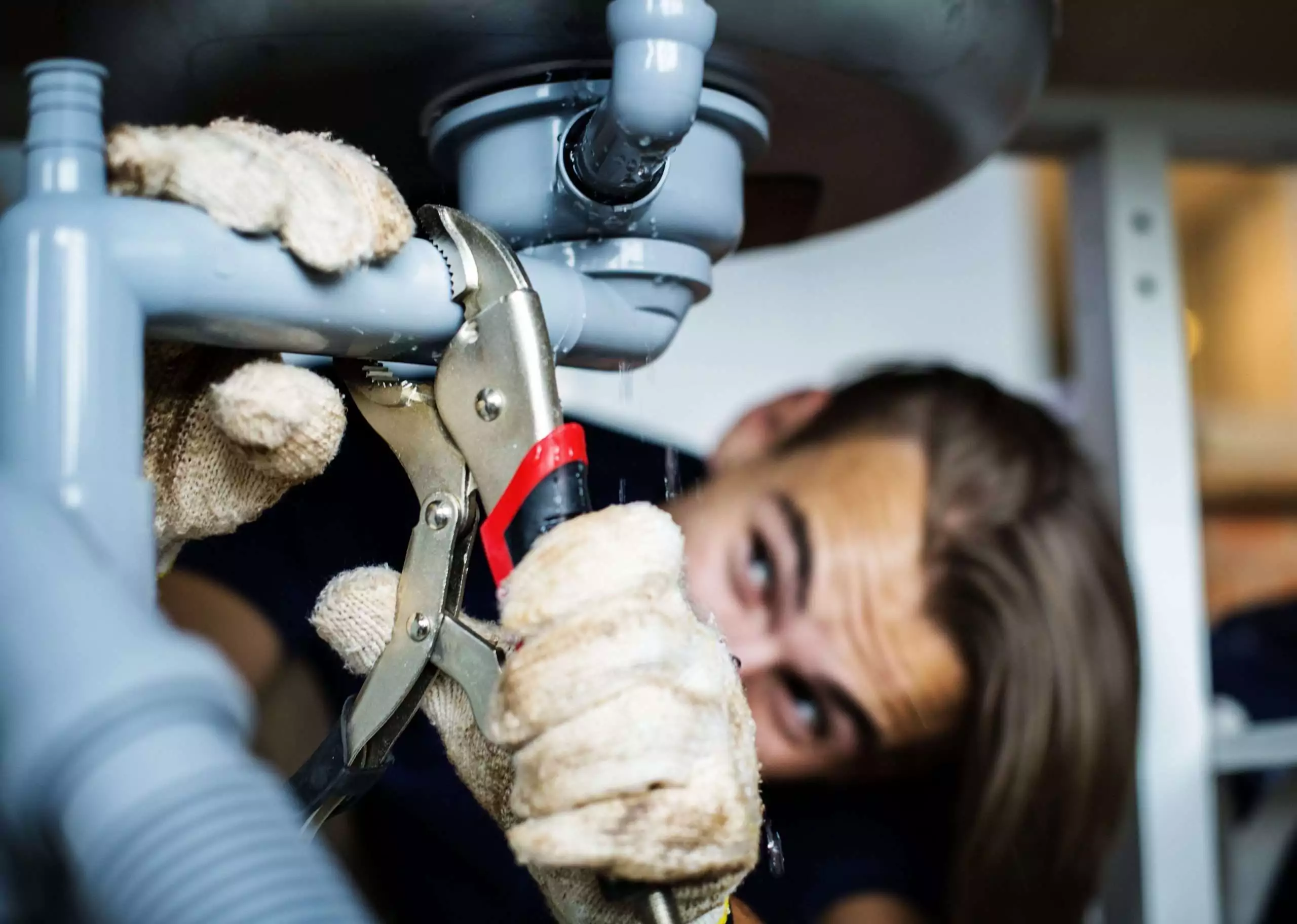 Man Repairing Leaky Pipe with Pliers Under Sink